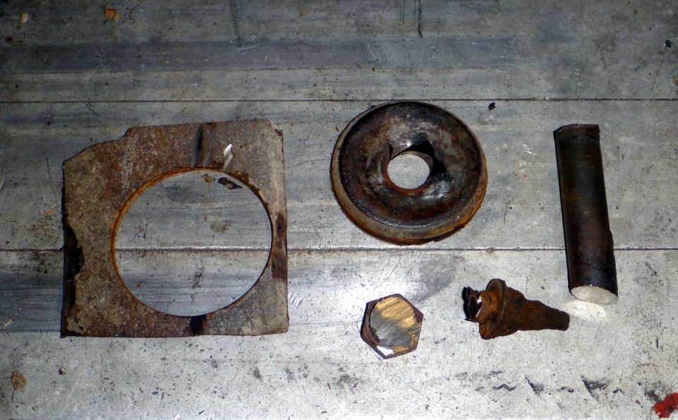 Several rusty metal parts including a bracket with a circular cutout, a washer-like piece, a bolt, and a cylindrical tube