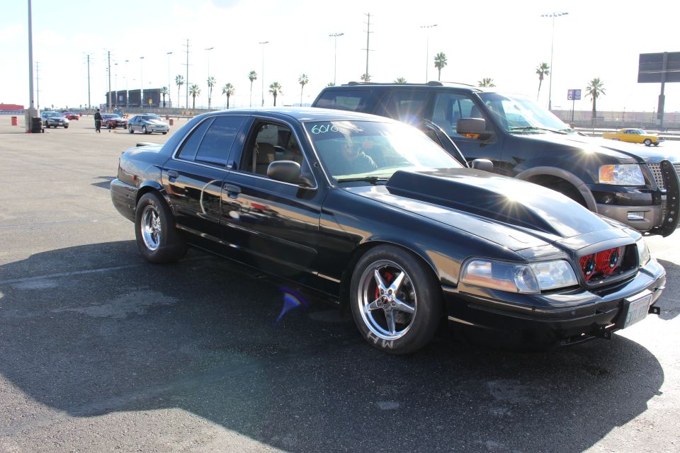 Black sedan with chrome wheels and SUV behind it in palm-lined parking lot