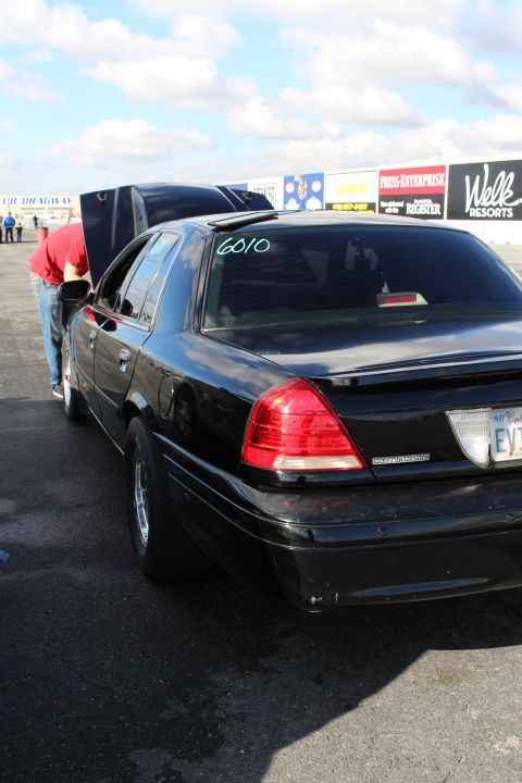 2003 Ford Crown Victoria - Rear three-quarter view of a black sedan with its hood open and the number 6010 written on the rear window.