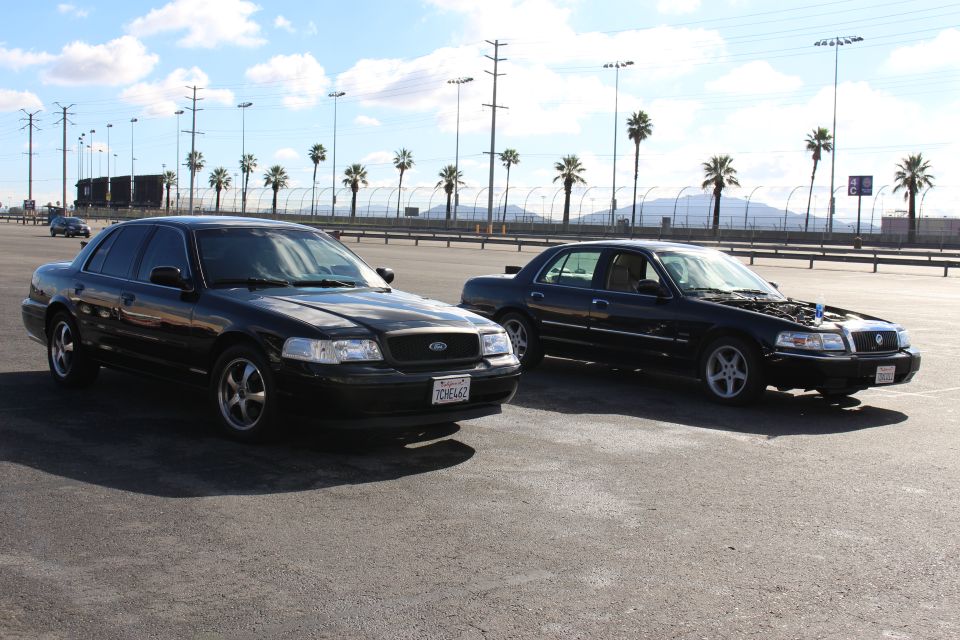 Two black Ford sedans parked at angles in a palm-lined lot under blue sky