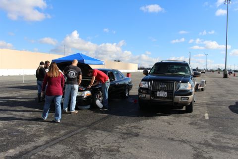 2003 Ford Crown Victoria - small group of people gathers around a black sedan with its hood open, parked next to a black Ford Expedition SUV.