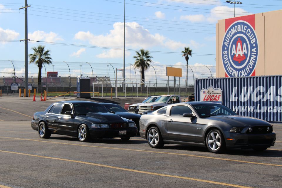 Black sedan and gray Mustang parked near AAA and Lucas Oil signs