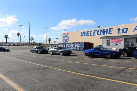 2003 Ford Crown Victoria - row of parked cars including Ford Mustangs and a blue sedan in a lot fronting a building with a large WELCOME sign.