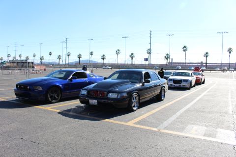 2003 Ford Crown Victoria - blue Mustang, black sedan and white Chrysler 300 parked in a sunny palm-lined lot with stadium lights behind.