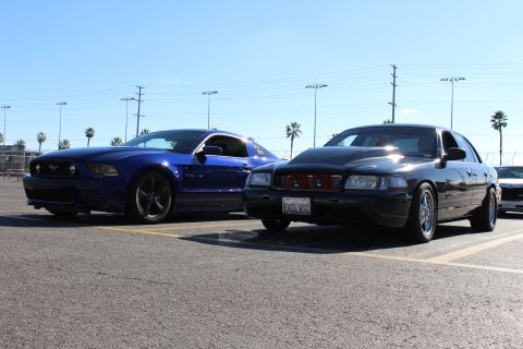 2003 Ford Crown Victoria - Front three-quarter view of a blue Ford Mustang beside a black Ford sedan showing red air filters behind its grille.