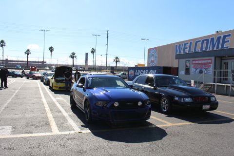 2003 Ford Crown Victoria - blue Ford Mustang and a black sedan sit in a parking lot in front of a building displaying a large WELCOME sign.