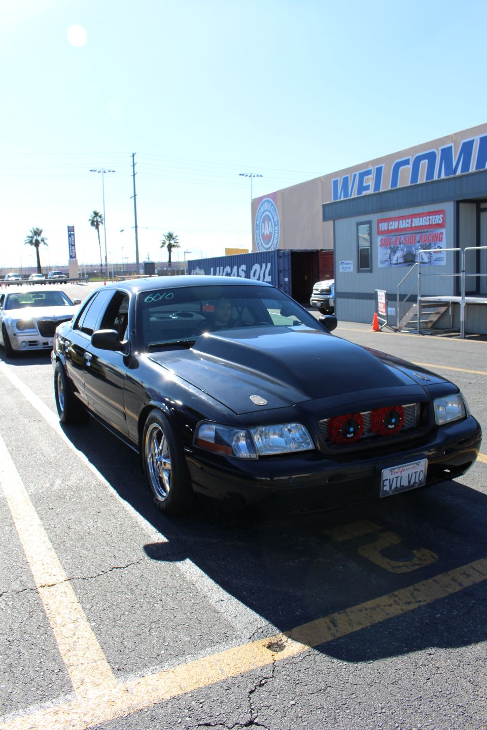 Black sedan with custom grille and EVIL VIC plate parked in front of a WELCOME building