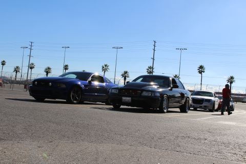 2003 Ford Crown Victoria - blue Mustang, black sedan and silver Chrysler 300 are parked in a sunny lot as a person in red walks past on the right.