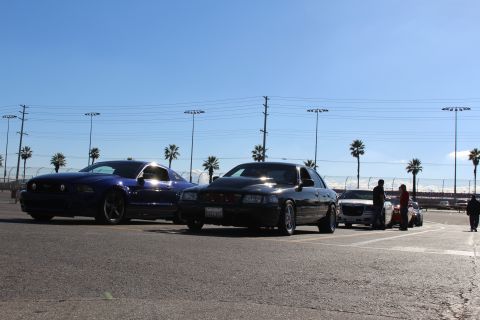 2003 Ford Crown Victoria - blue Mustang and a black sedan are parked beside a silver car as a couple of people stand near them in a sunlit lot.