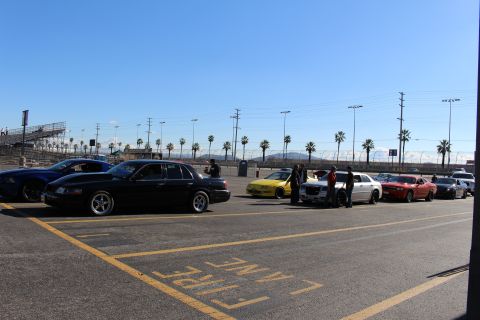 2003 Ford Crown Victoria - row of cars including a black sedan and sports coupes parked at a sunny dragstrip lot lined with palm trees and grandstands.