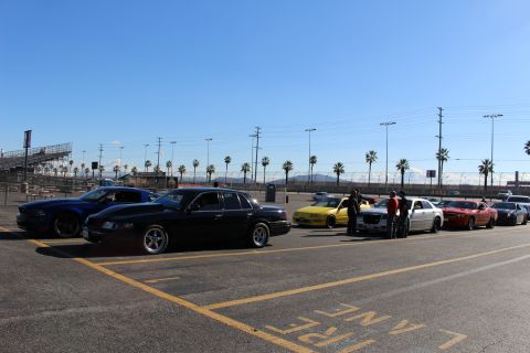 2003 Ford Crown Victoria - black sedan and a lowered dark coupe sit in a sunlit parking lot at a dragstrip, with cars and people staged behind them.