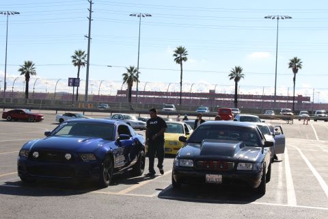2003 Ford Crown Victoria - blue Ford Mustang and a black Mustang are parked side by side as a man stands between them in a sunny dragstrip lot.
