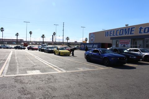 2003 Ford Crown Victoria - row of cars including a yellow sports car and a blue Mustang are parked outside a WELCOME building at a sunny dragstrip.