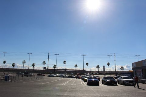 2003 Ford Crown Victoria - Distant rows of parked cars stretch across a vast sunny dragstrip lot lined with palm trees under a bright sun flare.