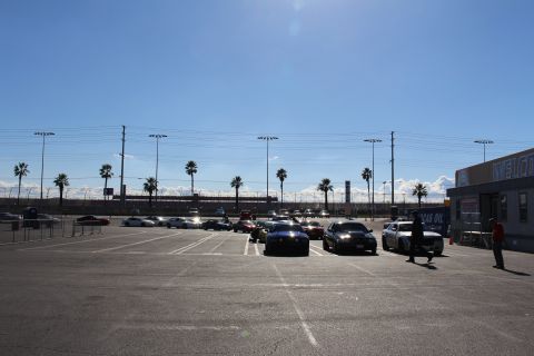 2003 Ford Crown Victoria - wide sunny parking lot holds parked cars and people walking, with a WELCOME building and Lucas Oil sign on the right.