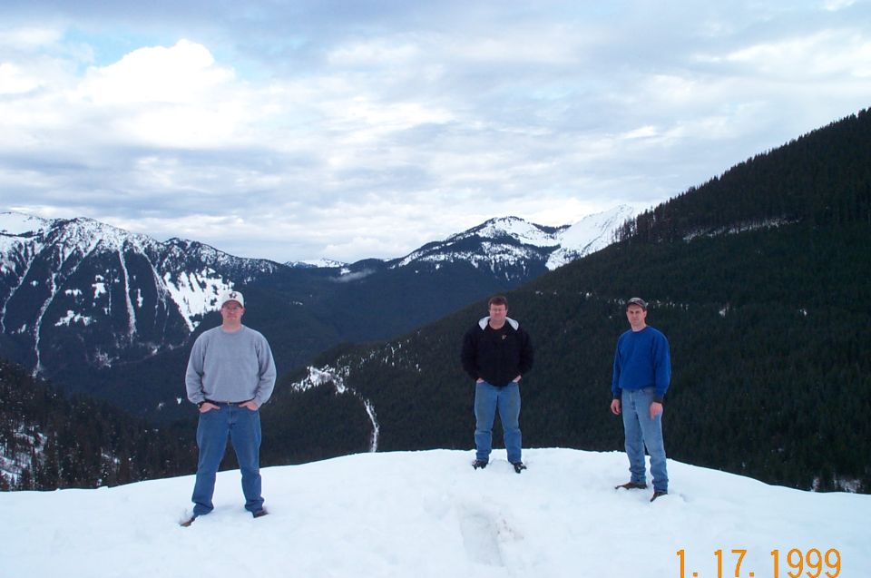 Three men on snowy ridge with mountains behind them