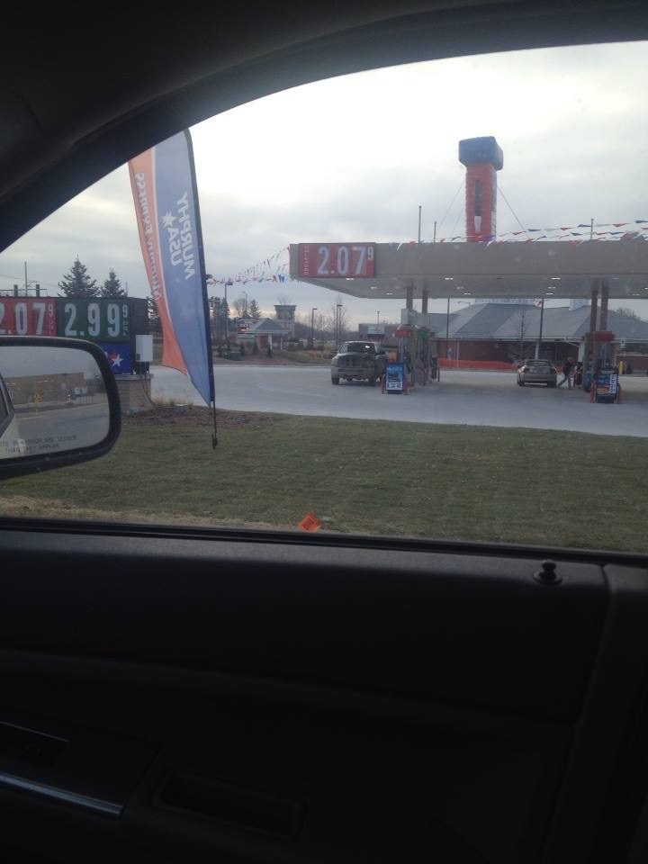 Gas station with price signs showing 2.07 and 2.99, viewed from inside a car