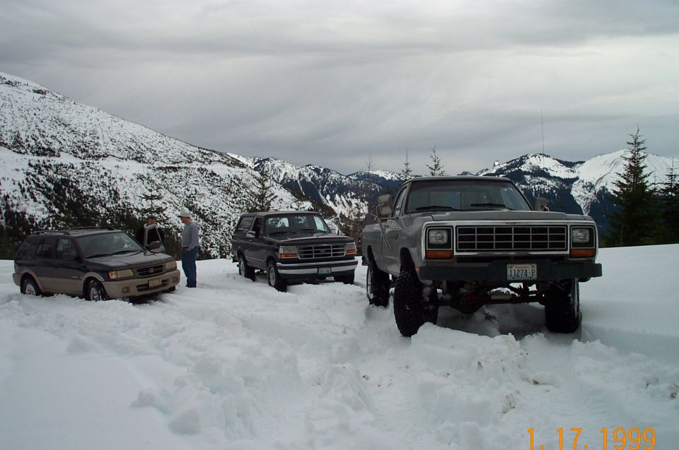 Three SUVs and trucks stuck in deep snow with snow-covered mountains behind them