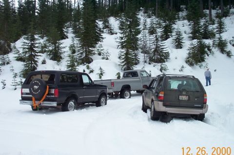 1995 Ford Bronco - Three vehicles are stuck in the snow on a wooded road.