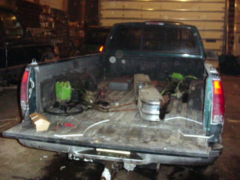 1992 Ford Bronco - Rear view of a green pickup truck bed filled with various parts and equipment.