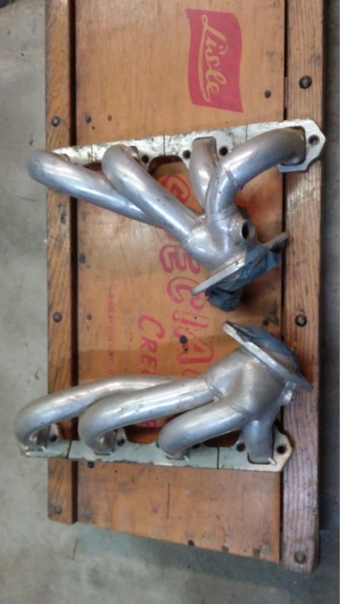 1995 Ford Bronco - Two exhaust manifolds are laid out on a wooden surface. The manifolds are made of shiny metal and appear to be for a V8 engine, with four p…