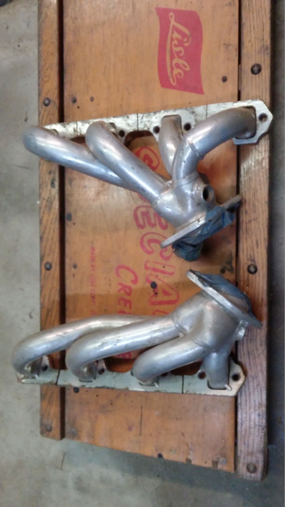 Two chrome exhaust manifolds on a wooden surface.