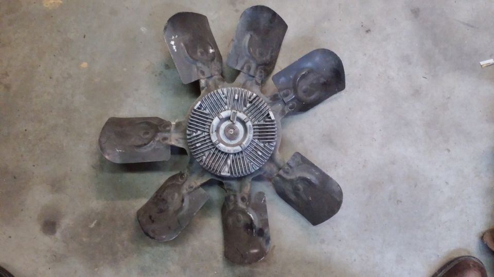 Black engine cooling fan with eight blades and silver hub on concrete floor.