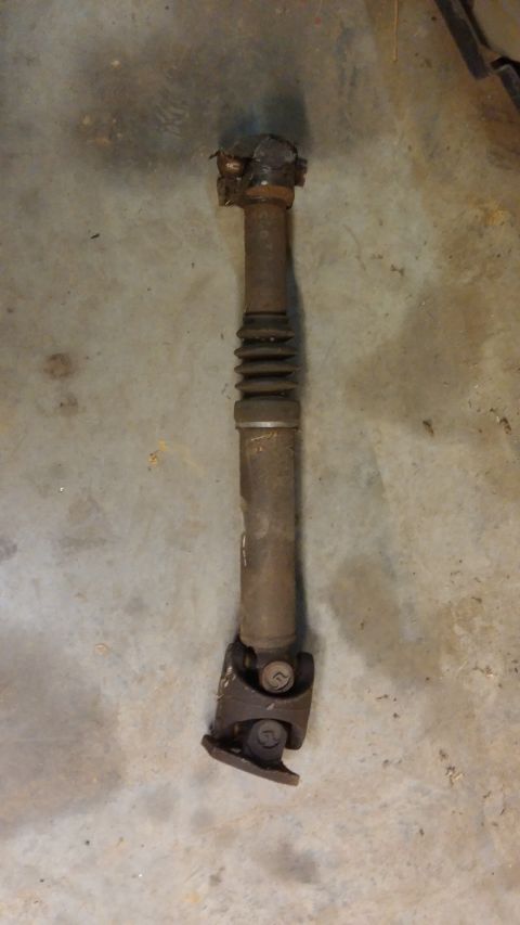 1995 Ford Bronco - A rusty driveshaft with two universal joints and a rubber boot is laid out on a concrete floor.