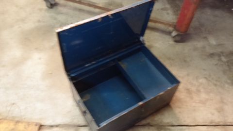 1995 Ford Bronco - An open, blue metal toolbox sits on a concrete floor. The toolbox has a divided interior and appears to be aged with some rust on the edges.