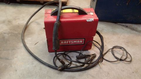 1995 Ford Bronco - A red Craftsman welder with a black handle and cables is on a concrete floor. The welder has the Craftsman logo on the front.