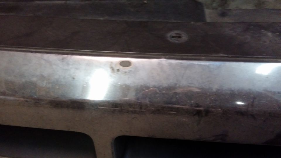 Close-up of a chrome vehicle bumper with two parking sensor holes and scuffs.