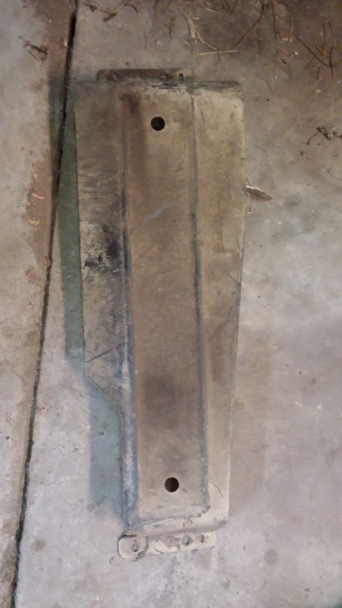 1995 Ford Bronco - A dusty, rectangular metal part with two visible holes is laid flat on a concrete surface. The part appears to be a component of a vehicle,…