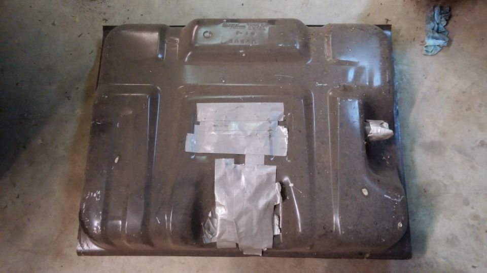 Underside of a dark fuel tank with silver tape repairs, possibly from a 1995 Ford Bronco.