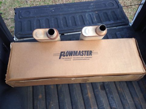 1979 Ford Bronco - A new Flowmaster exhaust muffler is shown in its cardboard box, placed in the bed of a pickup truck. Two used mufflers, one on either side…