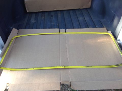 1979 Ford Bronco - A yellow metal trim piece, possibly a window gasket or molding, is laid out on cardboard in the bed of a pickup truck. The trim piece is cu…
