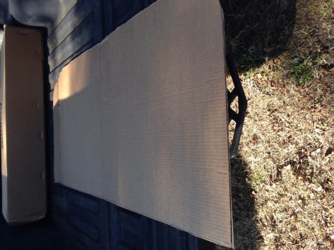 1979 Ford Bronco - A large piece of corrugated cardboard is laid out on a dark surface, possibly a truck bed, with dry grass and a metal object visible to the…