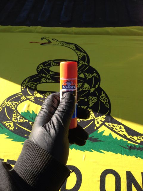 1979 Ford Bronco - A gloved hand holds an Elmer's glue stick in front of a yellow flag with a coiled rattlesnake and the words "DON'T TREAD ON ME" visible.