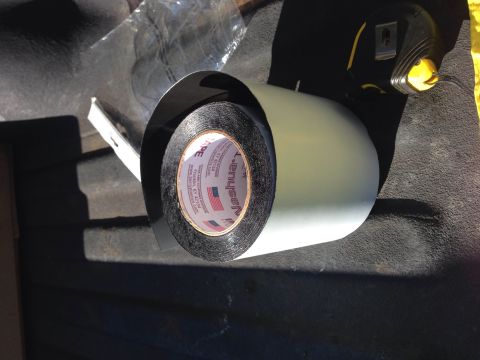 1979 Ford Bronco - A roll of black duct tape with a light gray backing is shown, partially unrolled. The tape is sitting on a dark textured surface, possibly…