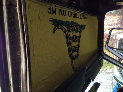 1979 Ford Bronco - The interior of a vehicle shows a Gadsden flag with a coiled rattlesnake and the words "DON'T TREAD ON ME" printed on it, covering the rear…