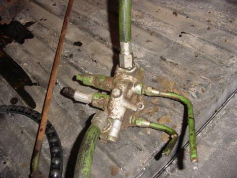 1992 Ford Bronco - A hydraulic valve assembly with green hoses is visible on a dirty, ribbed surface.