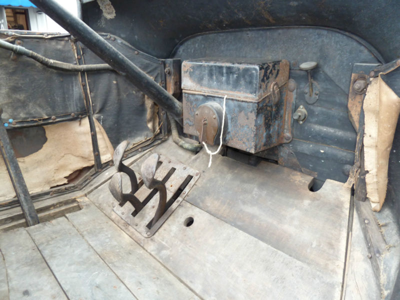 Interior of an old car with wooden floor, pedals, and a black metal box.