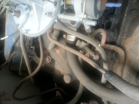 1973 Ford F-100 - A close-up view of an engine bay, focusing on the carburetor and various hoses and wiring. The engine block has some visible casting number…