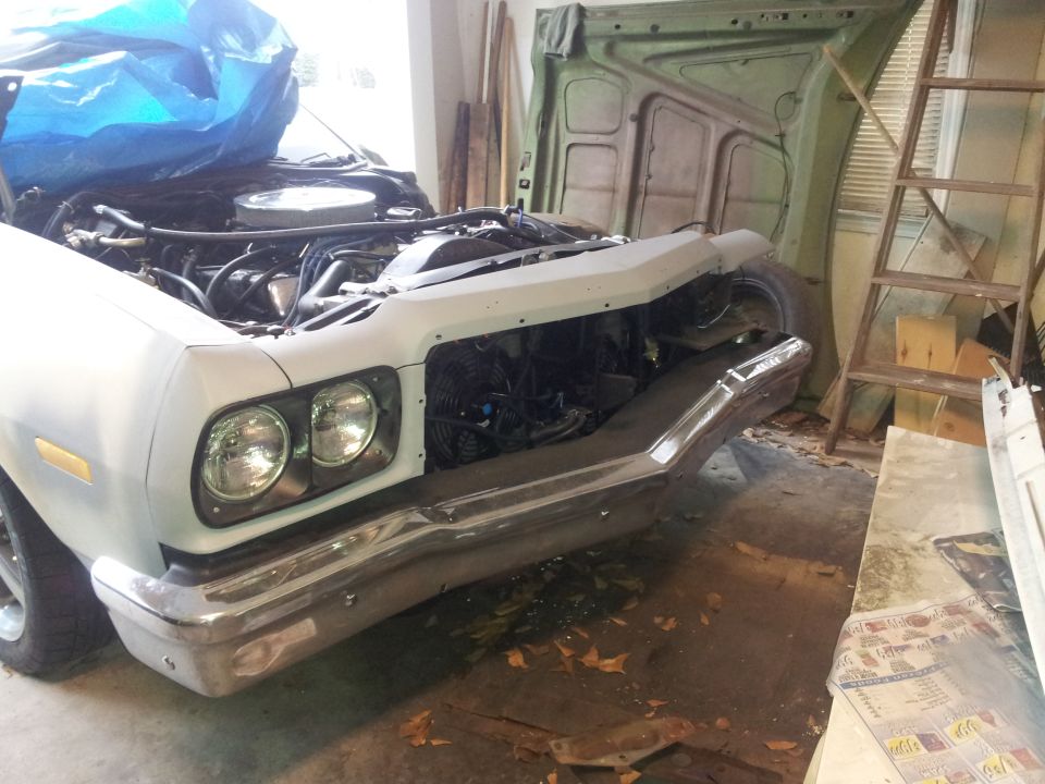 White 1970s pickup truck with hood open in a garage, showing engine and green hood in background.