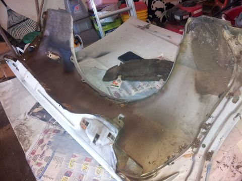 1976 Ford Ranchero - A heavily rusted and dirty car fender or wheel well liner is laid out on a table covered with newspapers. The part appears to be made of me…