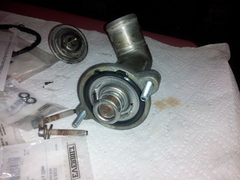 1976 Ford Ranchero - A disassembled engine thermostat and housing sit on a white paper towel. Several bolts and a gasket are also visible in the foreground.