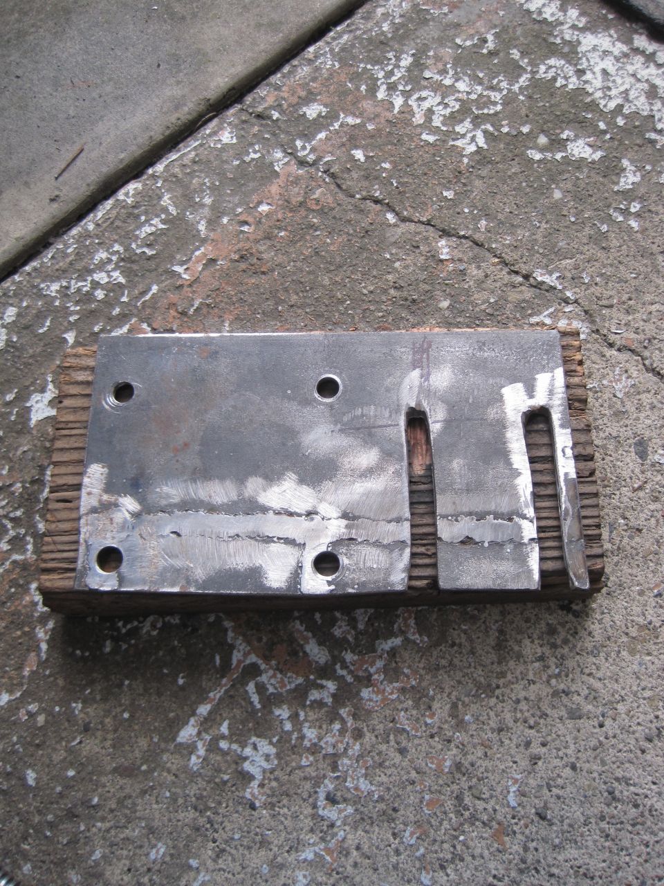 Photo of a fabricated steel mounting plate with bolt holes lying on concrete