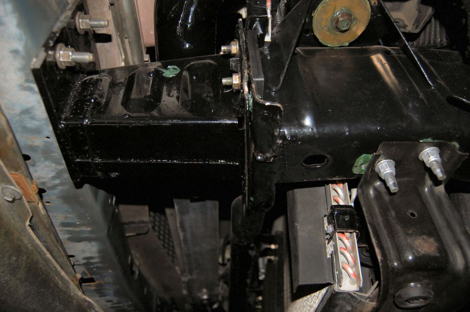 Underside view of vehicle chassis with black metal brackets, bolts, and wiring.