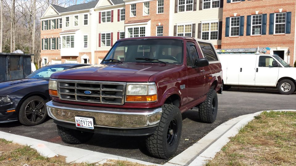 Maroon 1990s Ford Bronco with lifted suspension parked in front of townhouses.