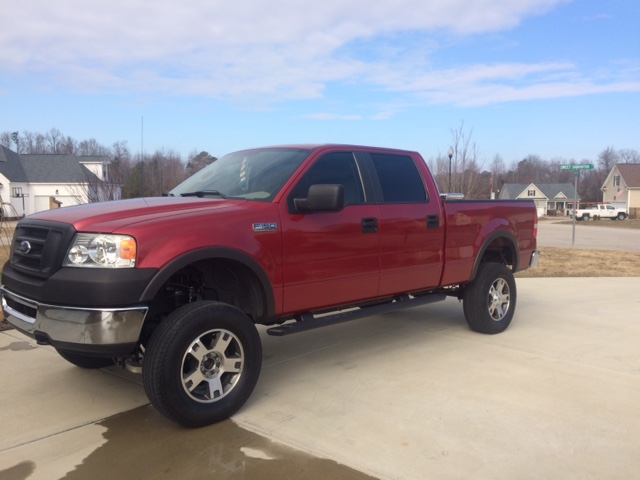 Red Ford F-150 pickup truck, lifted, with chrome wheels and running boards, parked on a driveway