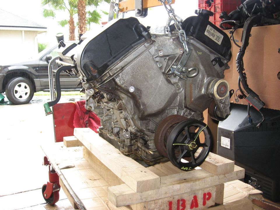 Engine on hoist, with a dark SUV visible in the background